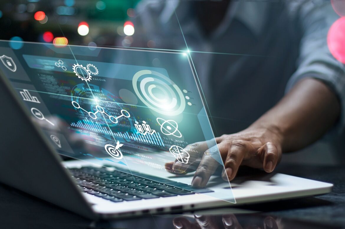 Fingers tipping on a laptop with a digital screen in front of it